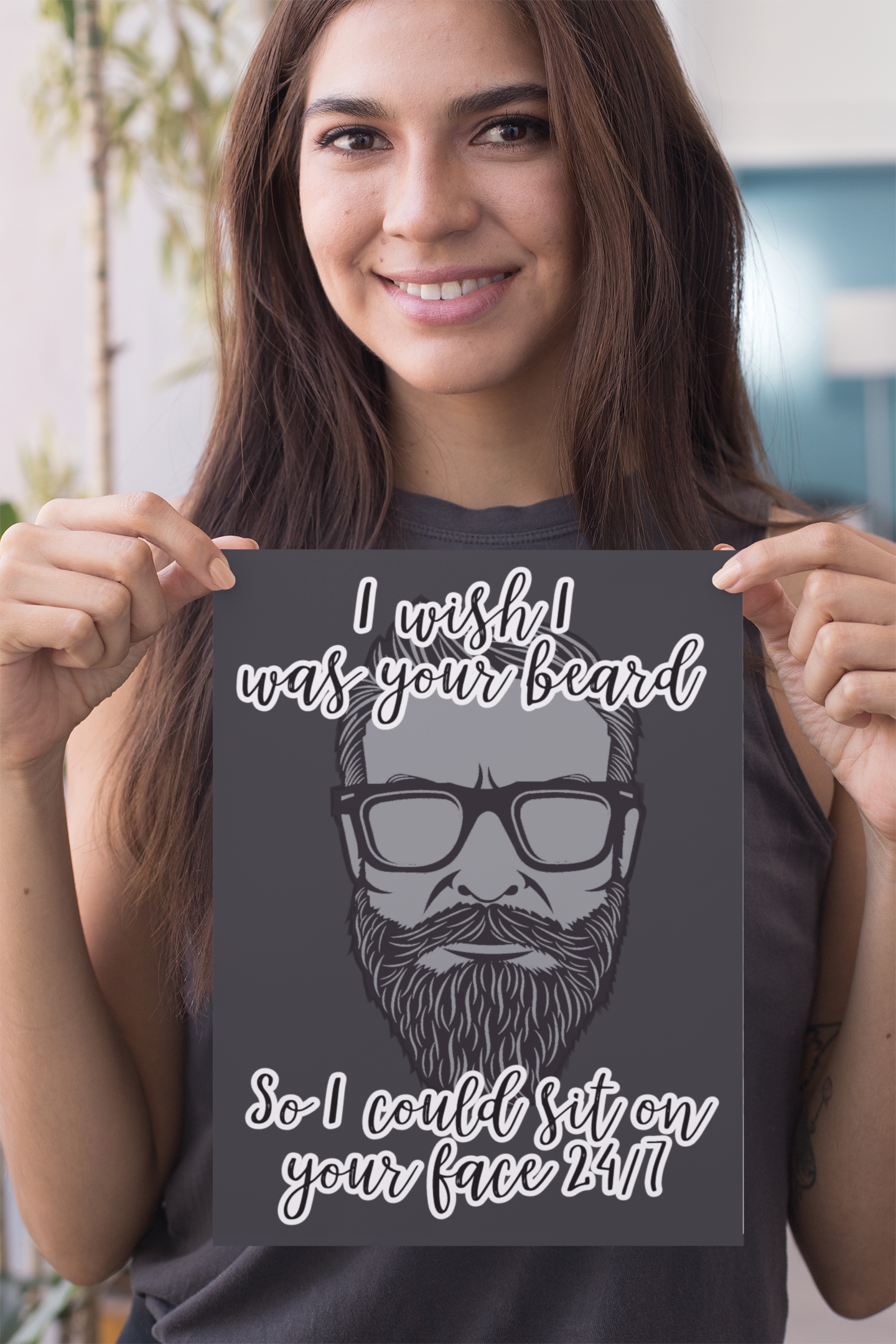 A woman holding a black vertical card featuring a clipart of a beard. To the top is the quote 'i wish i was your beard' and to the bottom ' so i could sit on your face 24/7. Printed in white.