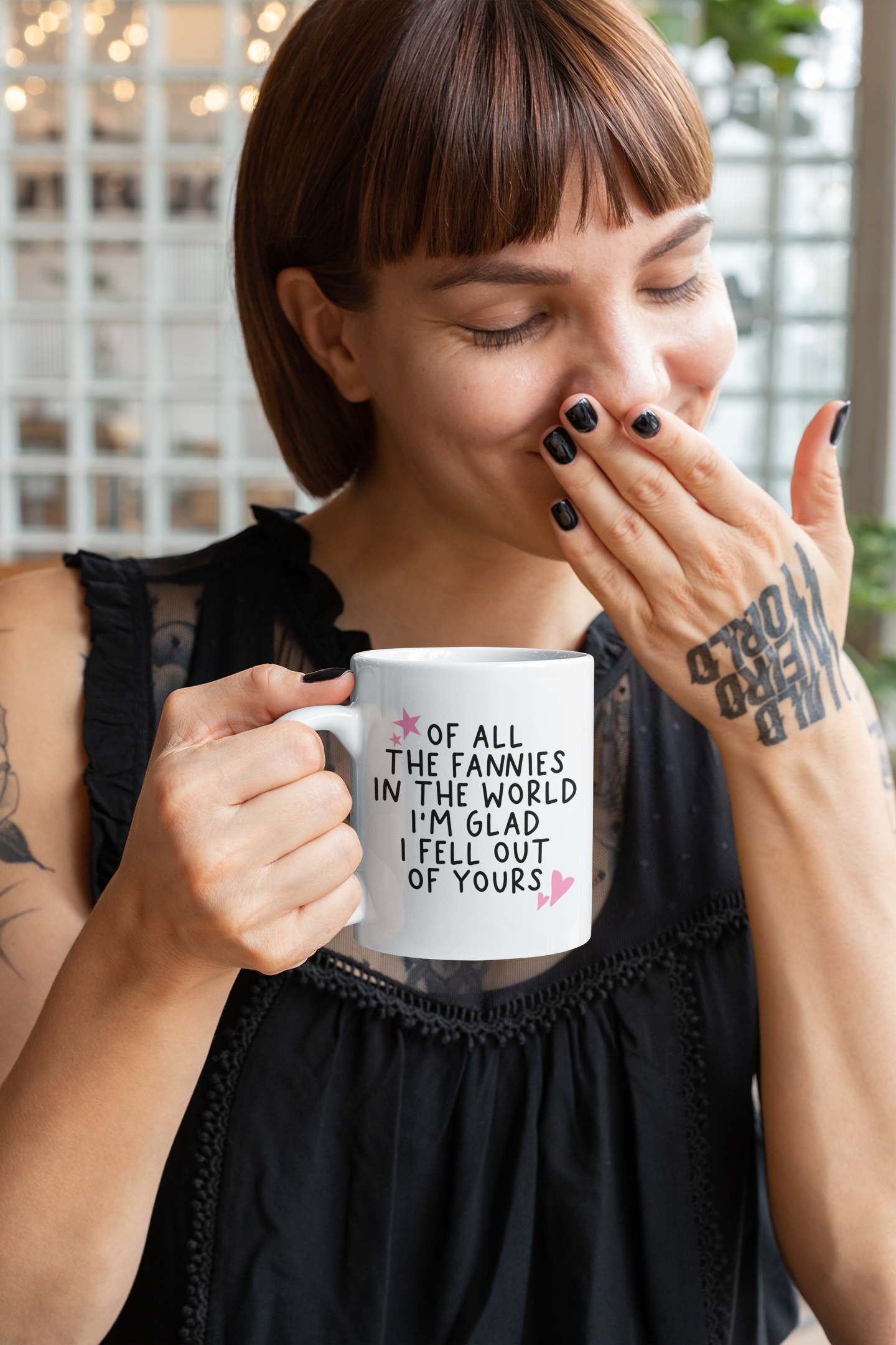 White ceramic mug with a funny quote 'of all the fannies in the world i'm glad i fell out of yours' in black ink. To the top left & bottom right of the text are little pink hearts and stars.