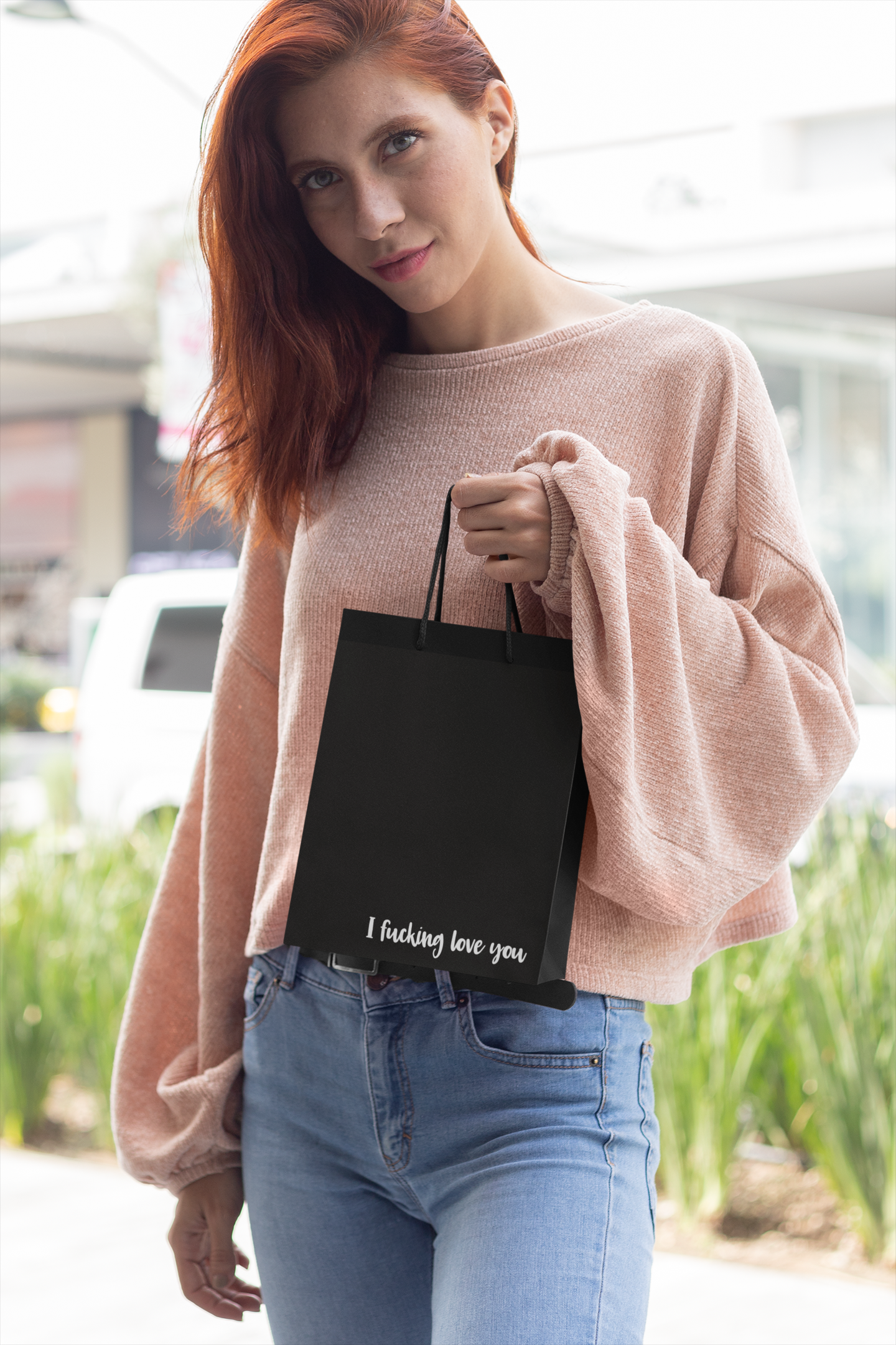 Woman holding a black gift bag featuring the quote 'i fucking love you' to the bottom right corner.