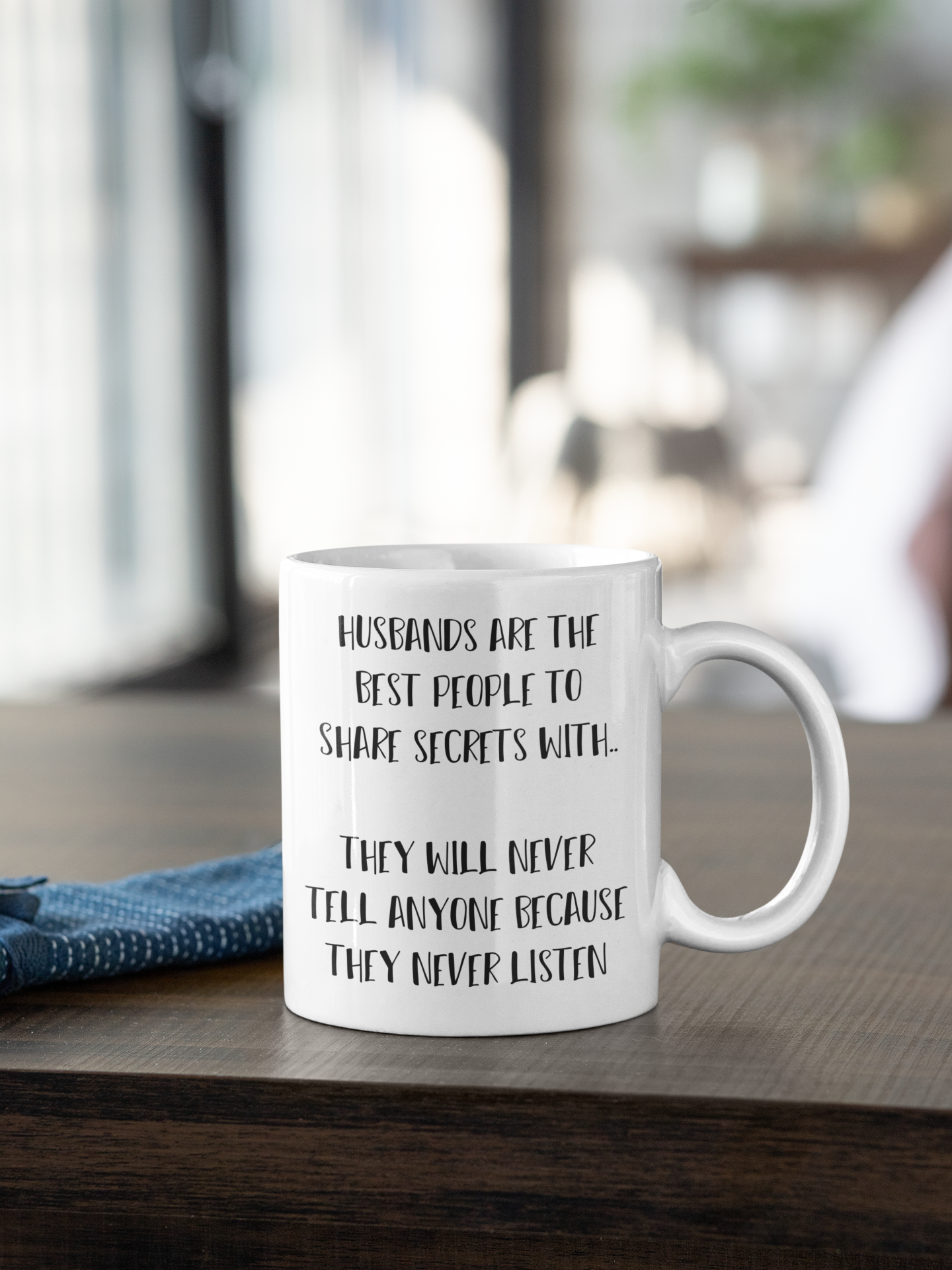 A white mug, featuring the funny quote 'husbands are the best people to share secrets with. They will never tell anyone because they never listen'. Printed in black ink.