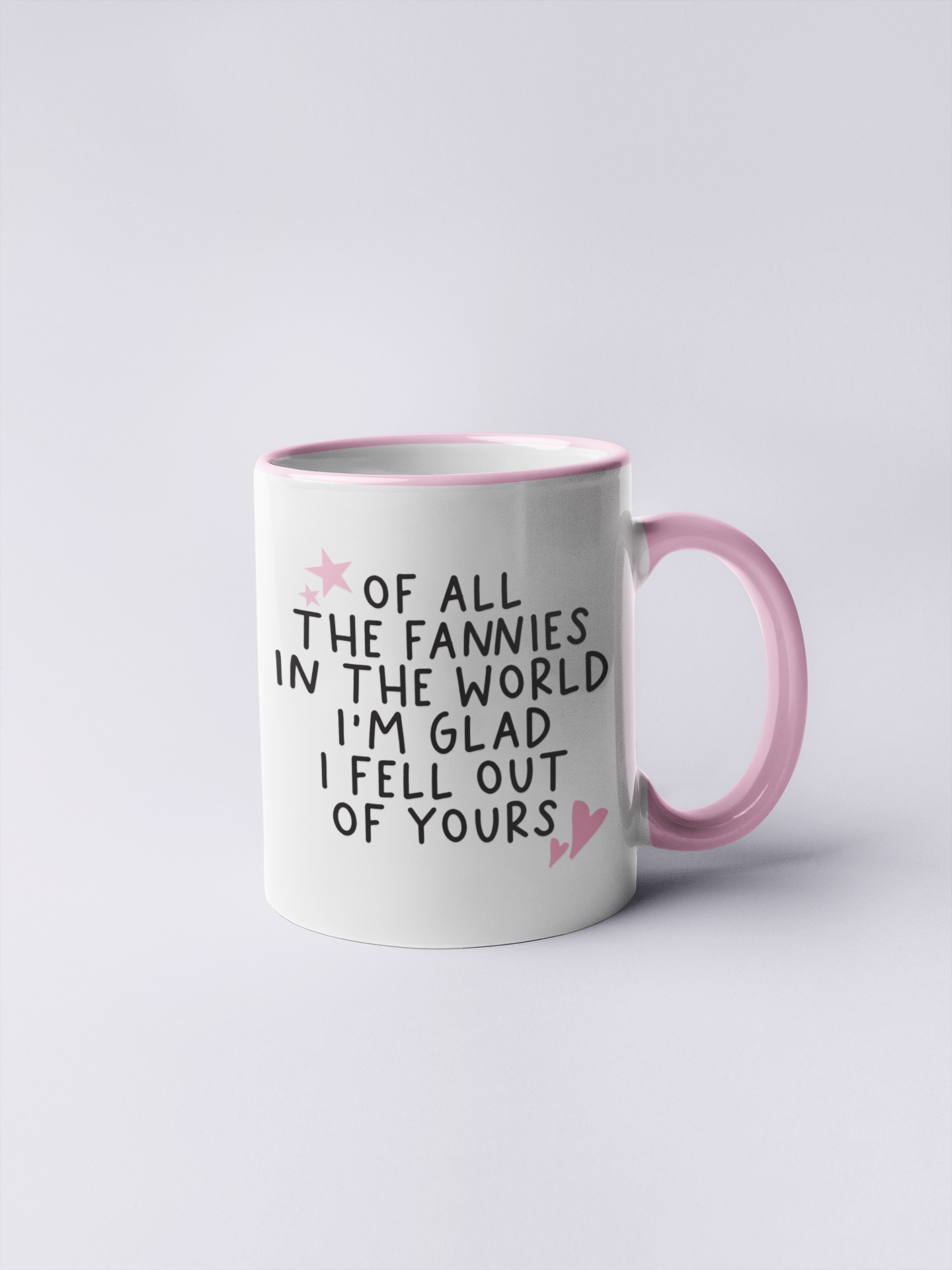 White ceramic mug with a funny quote 'of all the fannies in the world i'm glad i fell out of yours' in black ink. To the top left & bottom right of the text are little pink hearts and stars.