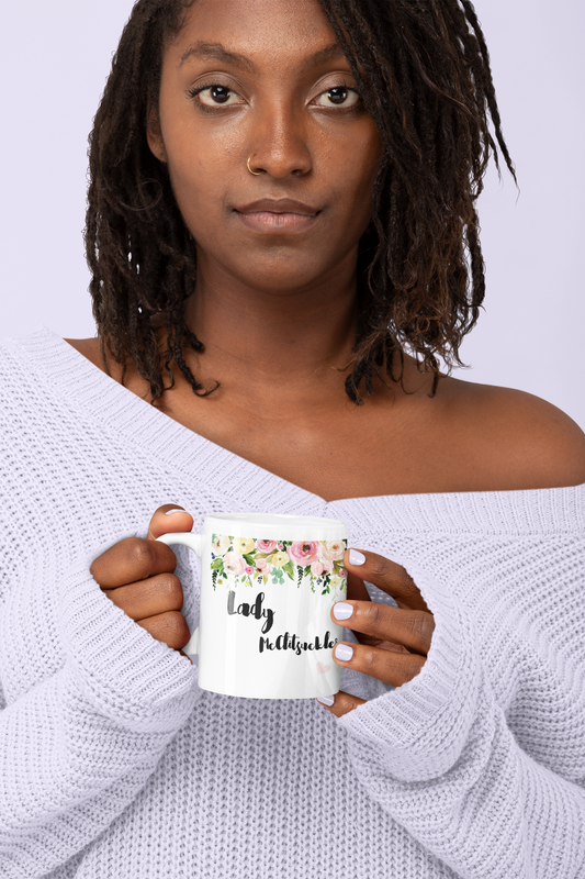 Woman holding a white mug with a colourful floral banner to the top. Under is a quote ' lady mcclitsuckler'.