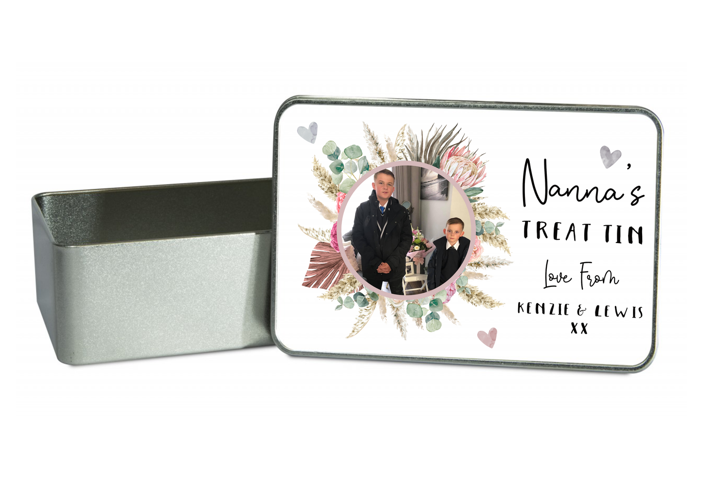 Square metal treat tin with a white slip lid. To the front of the lid it has a colourful floral design wreath with a personalised photo of 2 children in the middle. To the right of the flower is the words 'nanna's treat tin, love...'. Printed in black ink.