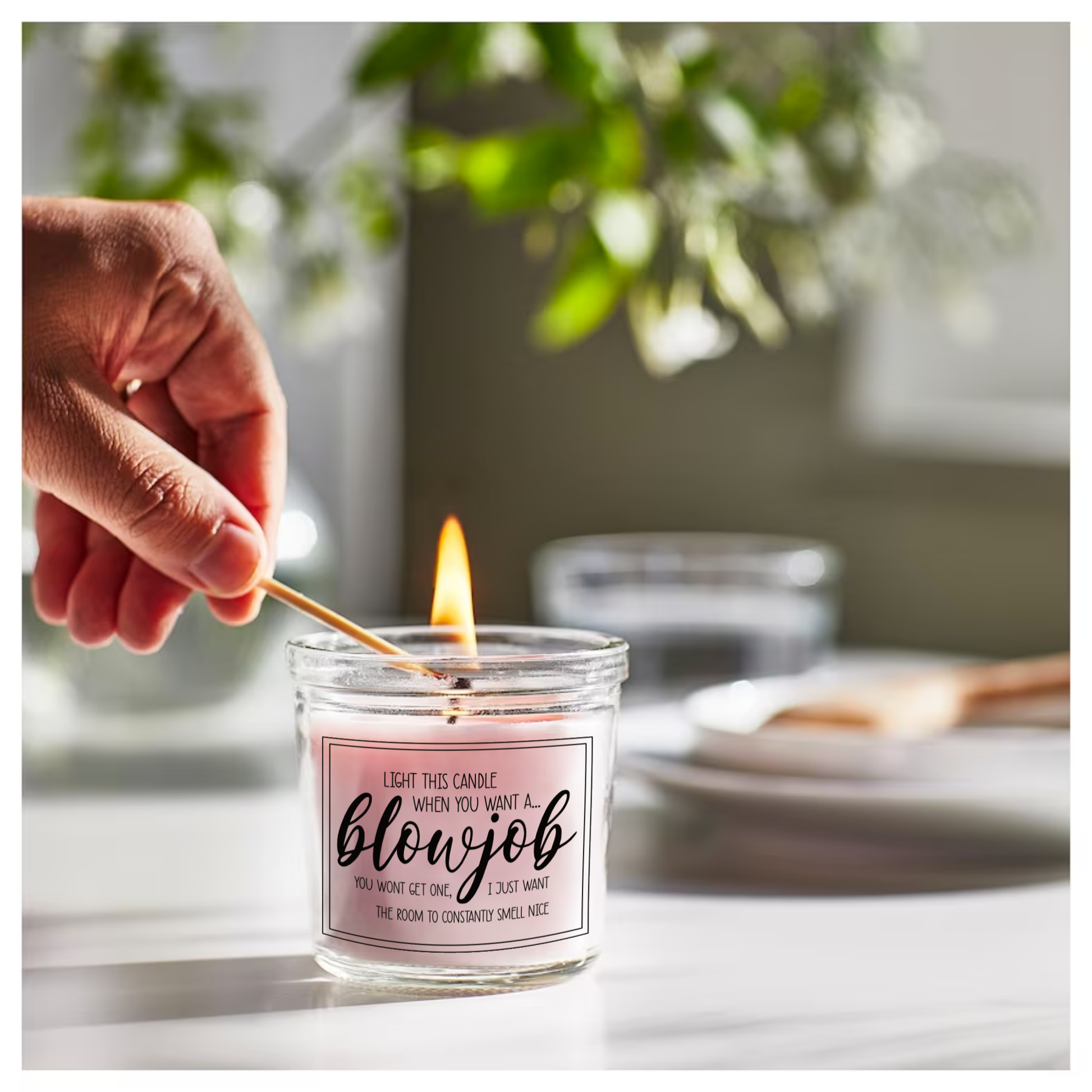 Glass jar candle with pink wax. Clear label to the front features a funny quote which reads 'light this candle when you want a blowjob. You won't get one, i just want the room to constantly smell nice'. 