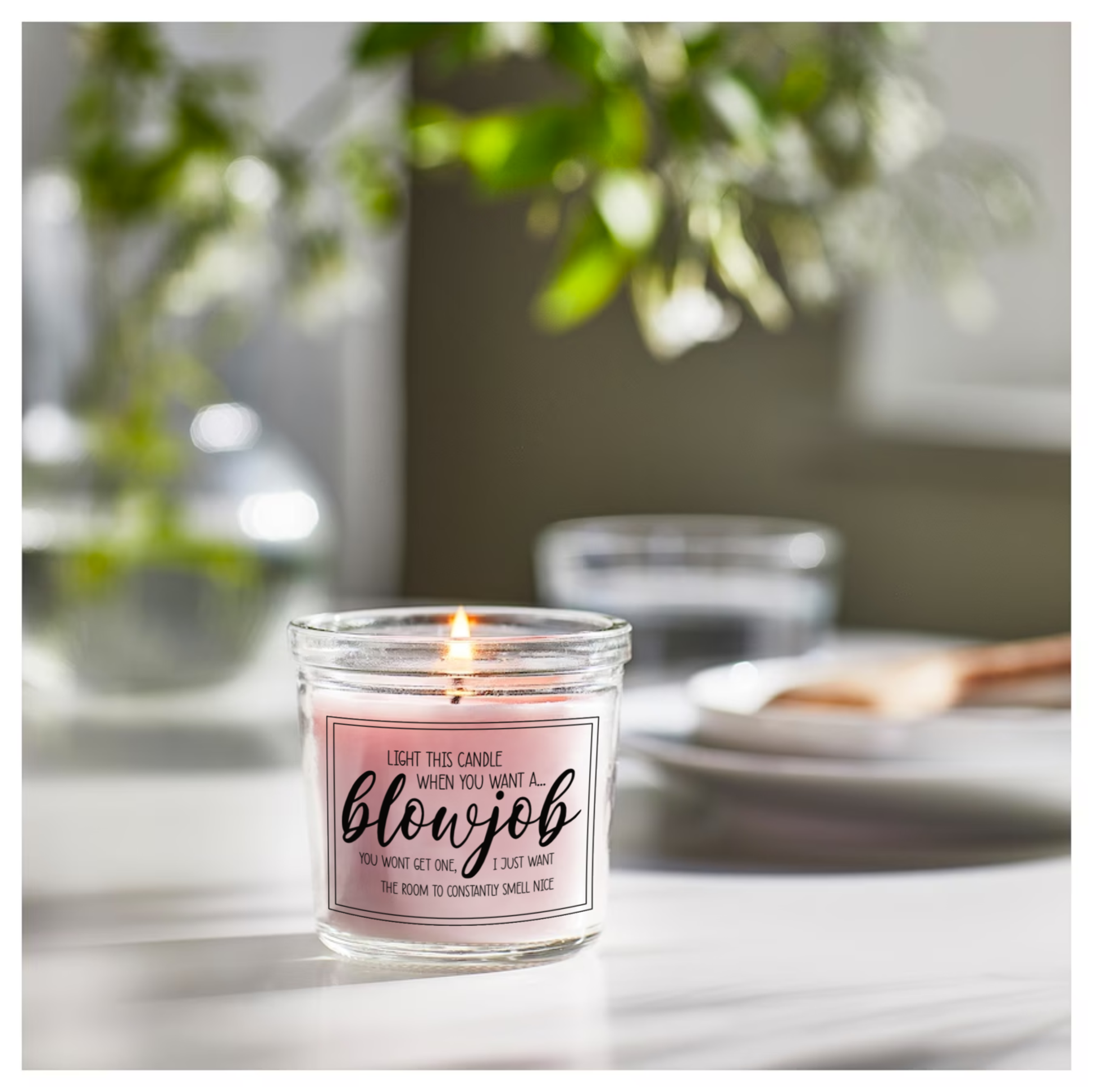 Glass jar candle with pink wax. Clear label to the front features a funny quote which reads 'light this candle when you want a blowjob. You won't get one, i just want the room to constantly smell nice'. 