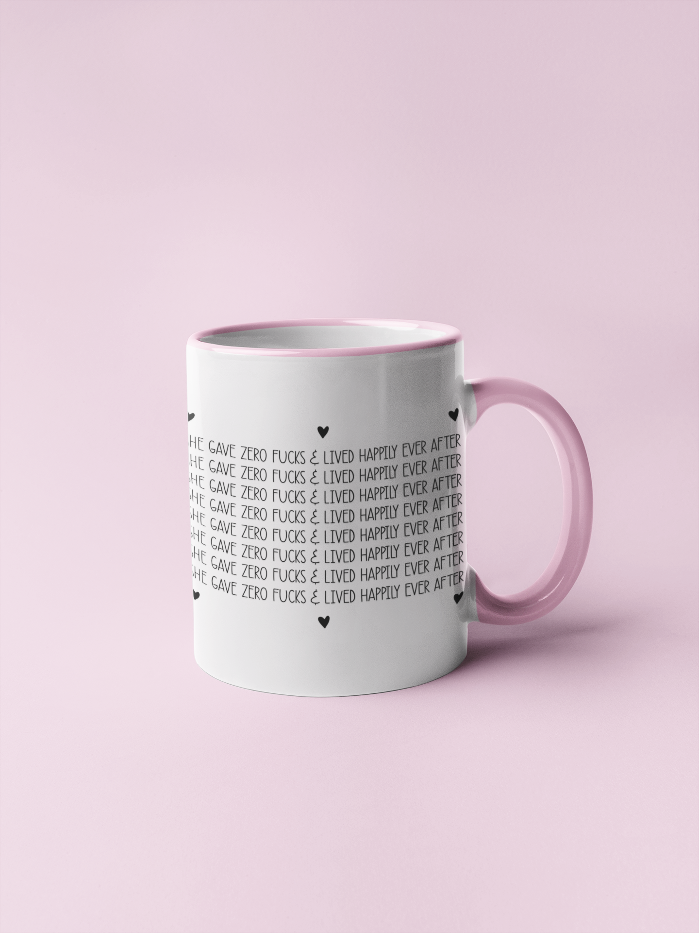White mug with a pink handle & rim with a repetitive design which says she gave zero fucks and lived happily ever after, with black  hearts surrounding the design.