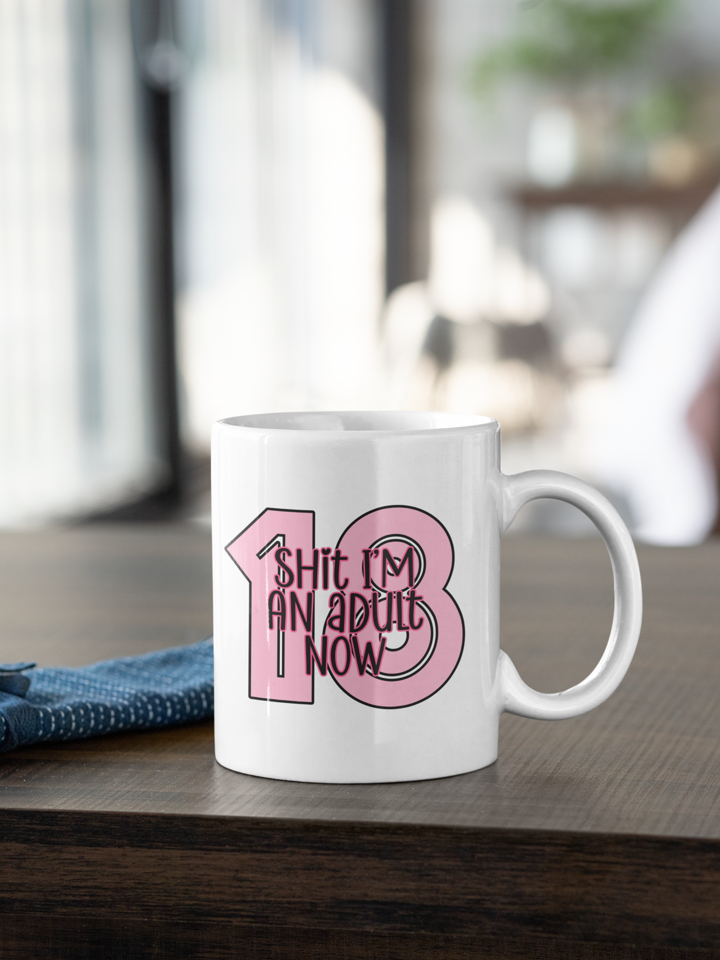 White mug with a bold 18 in baby pink and over the top it reads shit i'm an adult now