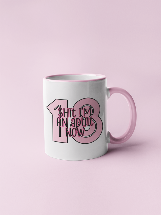 White mug with a pink handle & inner. To the front is a bold 18 in baby pink and over the top it reads shit i'm an adult now