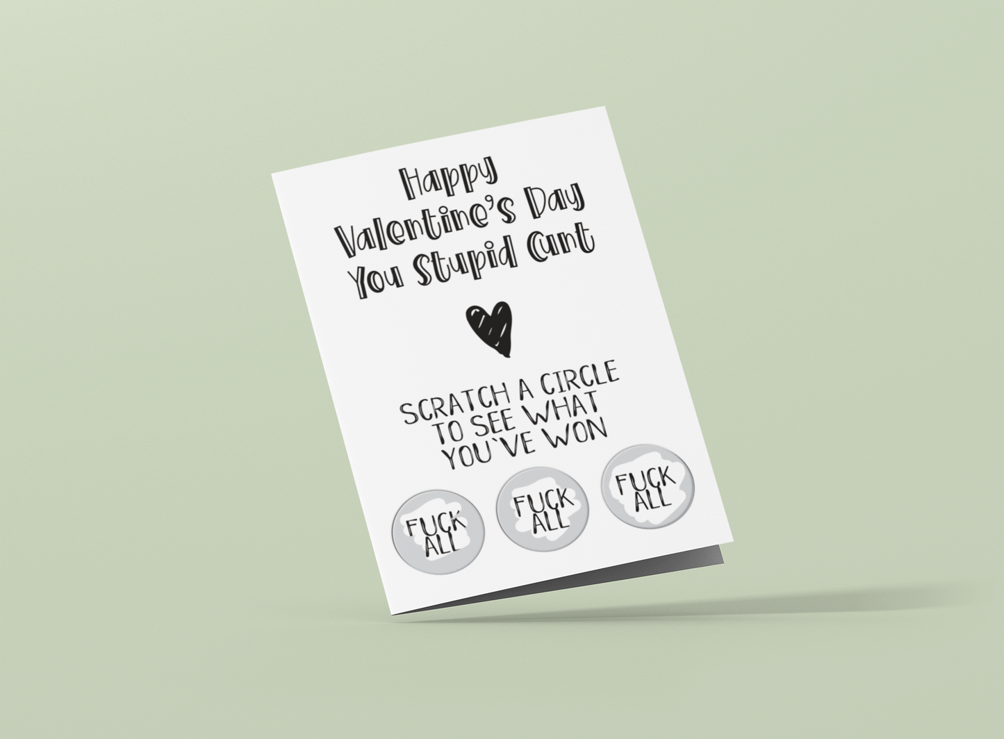 White vertical greetings card saying 'happy valentine's day you stupid c*nt' with a heart underneath. Then below is 'scratch a circle to win a prize'. To the bottom are 3 scratch stickers revealing the prizes. All printed in black ink.
