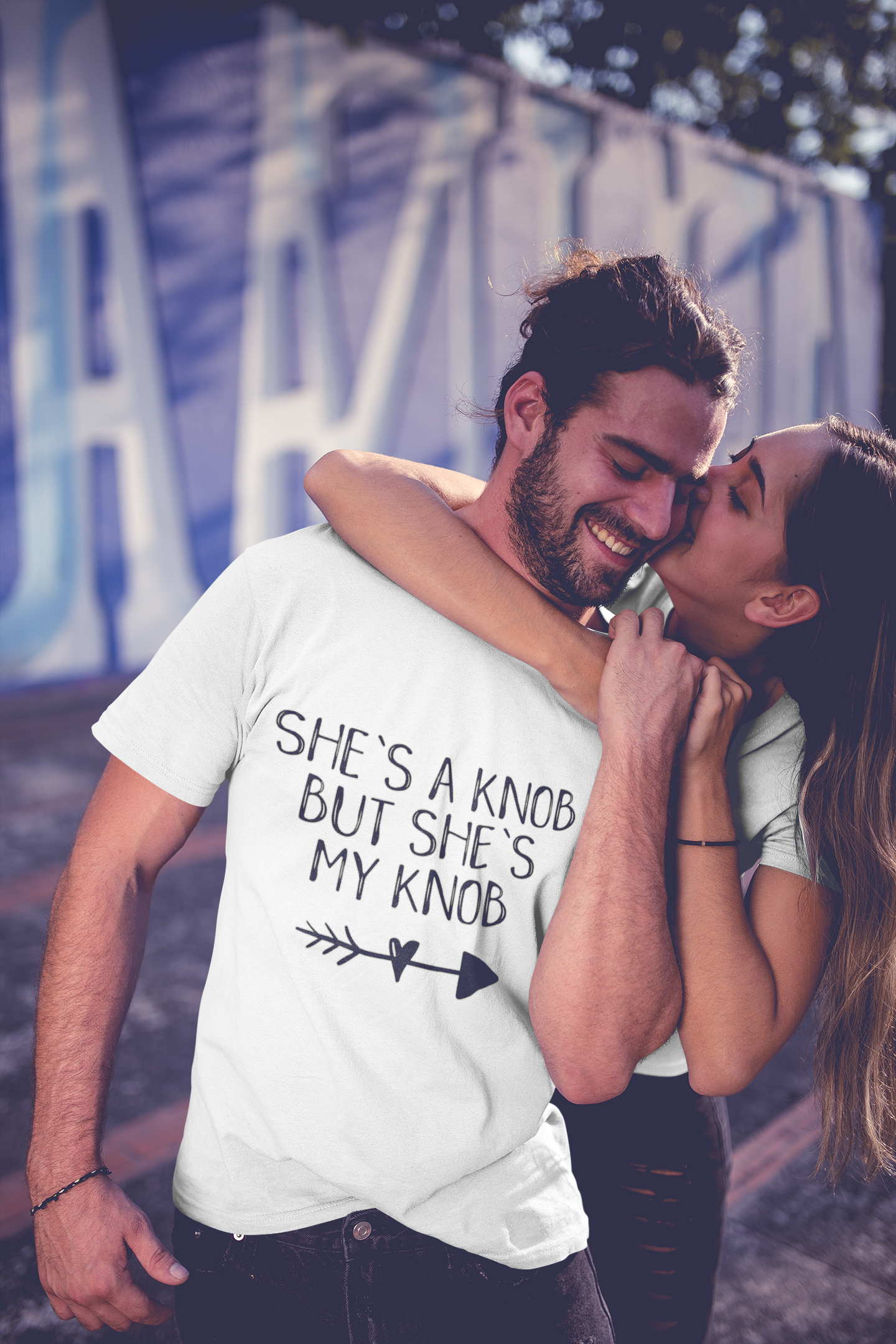 A man wearing a white t-shirt with the funny quote 'she's a knob but she's my knob'. Printed in black ink.