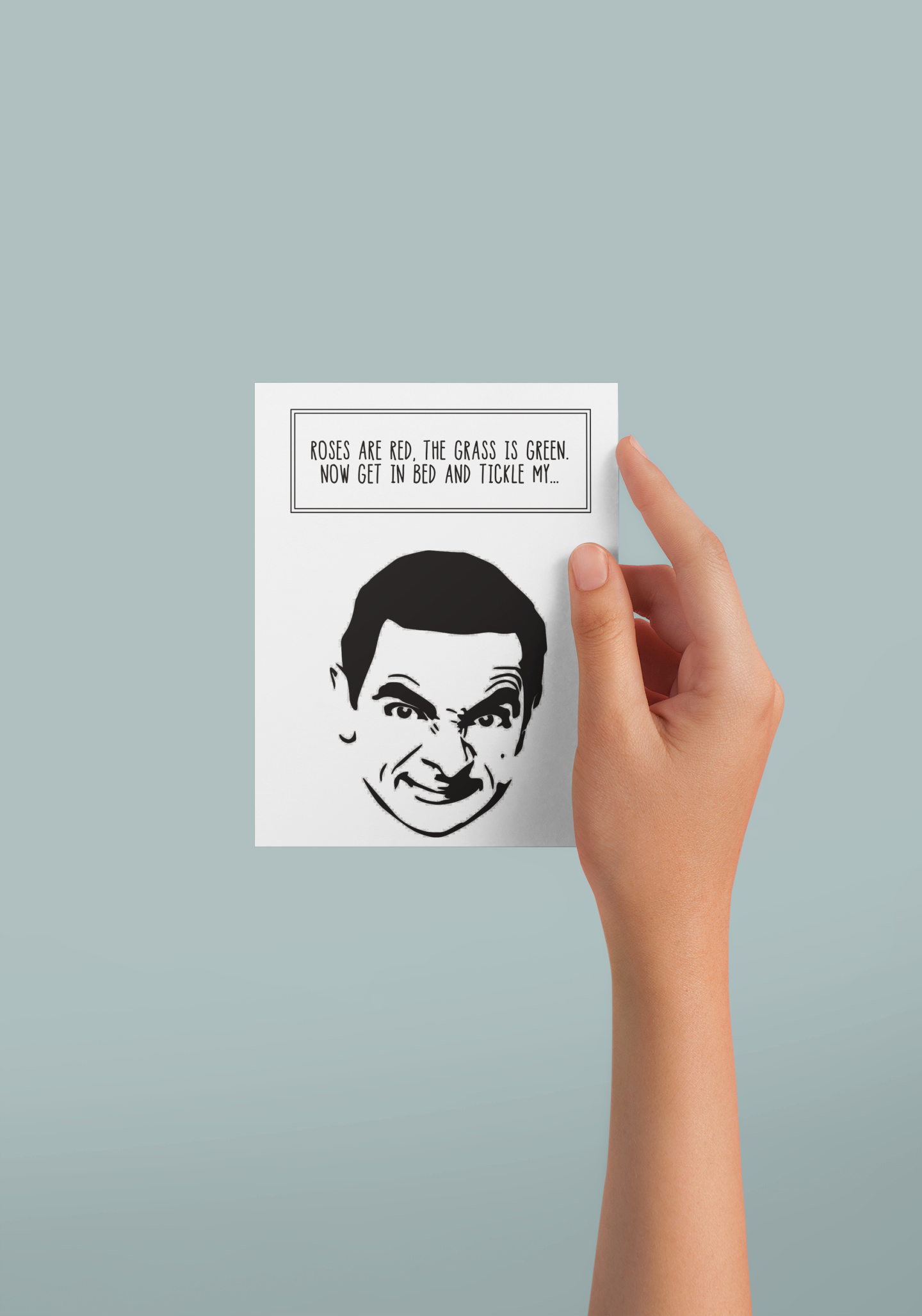 Hand holding a vertical greetings card featuring a silhouette of Mr Bean. To the top it reads 'roses are red, the grass is green, get in bed & tickle my...'. Printed in black ink.