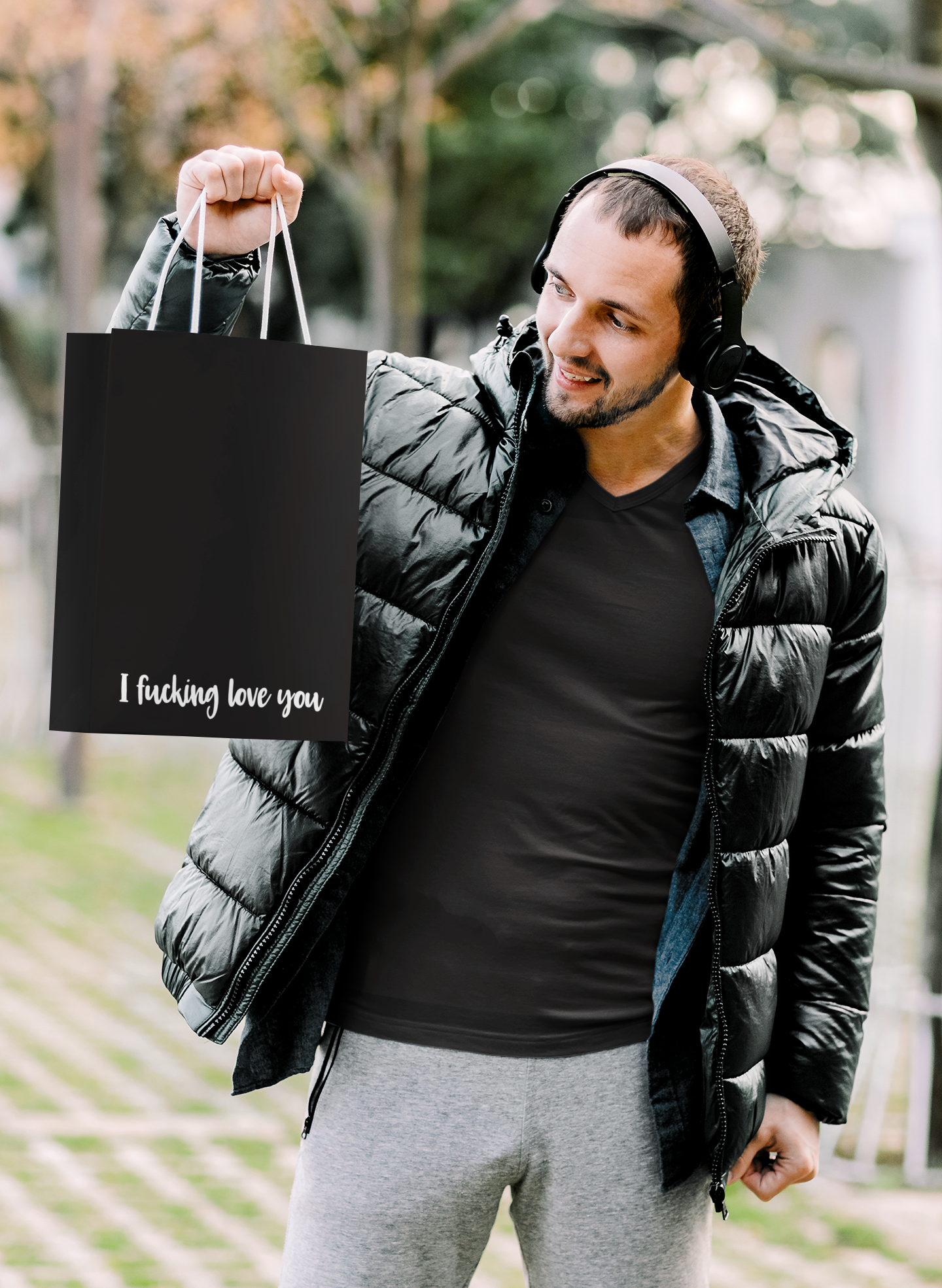 Man holding a black gift bag featuring the quote 'i fucking love you' to the bottom right corner.